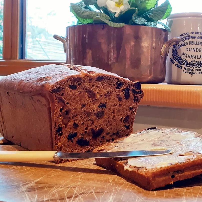 Sliced homemade fruit loaf with butter on wooden board
